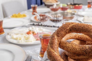 Simit, simit adlı Türk simidinin yakın plan fotoğrafını çek. Seçici odaklanma, bulanık geleneksel kahvaltı masası düzeneği. Misafir bekliyoruz, fotoğrafta kimse yok. Peynir, bardak çay, salam, kavanoz, domates, zeytin