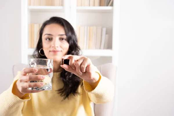 stock image Vitamin pill, portrait of happy woman looking camera holding vitamin pill and glass of fresh pure water. Casual dress at home, selective focus, copy space. Close up healthy lifestyle concept idea.