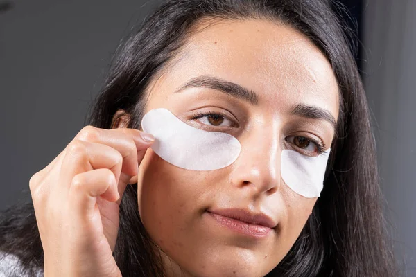 Under eye patch, close up no make up, natural face using under eye patch. Caucasian brunette millennial woman, fight with dark circles. swelling and wrinkles, wellbeing concept idea photo.