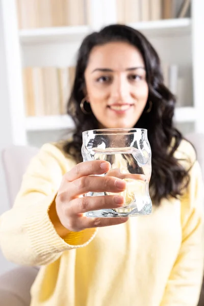 Offering glass of water, selective focus and blurry background of woman offering glass of water. Happy young sincere girl showing fresh aqua. Daily hydration health care concept idea, copy space image