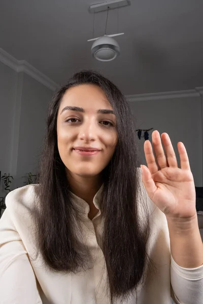 Woman waving hand, head shot portrait of happy millennial woman waving hand. Hello or bye at smartphone camera. Video call concept idea. Smiling freelance employee or businesswoman making video call.