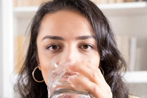 Drinking water, close up cropped image of woman drinking water. Happy beautiful caucasian thirsty woman holding transparent glass in her hand. Selective focus on her eyes, health and skin care concept