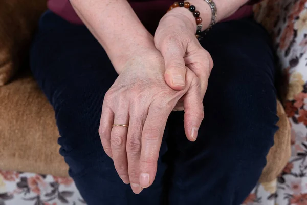 Hand pain of old woman, close up image of hand pain of old woman. Suffering from pain. Caucasian older lady sitting at home and massaging her self. Applying moisturizing cream, easing aches.