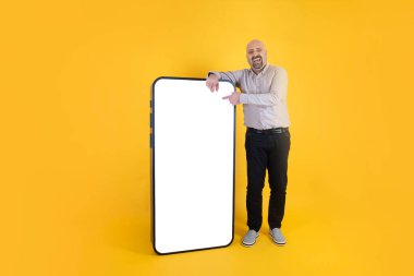 Büyük akıllı telefon, gülen beyaz adam büyük akıllı telefona eğiliyor. Sosyal medya uygulamasında komik resim ya da video gösteriliyor. Model için boş beyaz ekran. Kopyalama alanı olan sarı arkaplan.