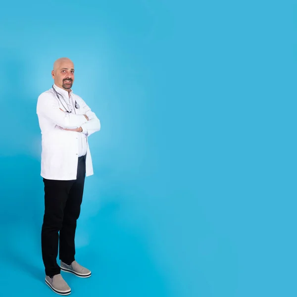 Middle aged male doctor, portrait of trusted middle aged male doctor. Physician in white coat with stethoscope, arms crossed on chest over blue background square image with copy space. Medical concept