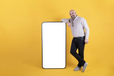 Mobil uygulama reklamı, mobil uygulama reklamları için akıllı telefonlara yaslanan adam. Kocaman beyaz ekranlı cep telefonunun yanında gülümseyen orta yaşlı bir erkek. Boşluğu kopyala.