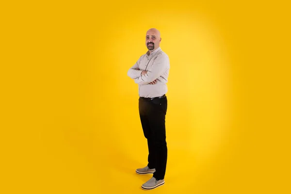Full body portrait of man, bald middle aged smiling full body portrait of man. Isolated yellow background, copy space. Casual dressed positive father figure male, arms crossed. Proud, confident guy.