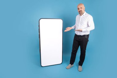 Mobil uygulama reklamı, Kafkas kel orta yaşlı adam yeni mobil uygulama reklamı öneriyor. Koca akıllı telefon ekranı boş, tam vücut çekim erkek, maket yap. İzole edilmiş mavi arkaplan, kopyalama alanı.