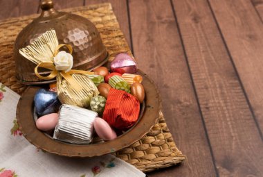 Bir kase şeker, antika bakır şeker kasesinin görüntüsü. Tahta masaya sarılmış çikolata ve badem sürahisi. Uzayı kopyala Bir sürü renkli ikram. Ramazan ziyafeti için metin alanı.