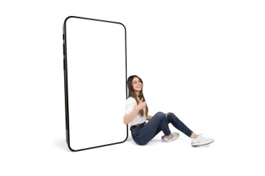 Oturan ve büyük akıllı telefonu boş beyaz ekran maketi ile eğilen bir kadın. Kameralar gülümsüyor, başparmaklar yukarı. Genç esmer kız öneriyor, mobil uygulama öneriyor..