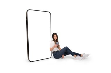 Akıllı telefon kullanan bir kadın. Dev cep telefonunun yanında oturuyor. Model için beyaz ekran boş. Tüm vücut boyu stüdyo çekimi. Web sitesi, uygulama önerme reklam kavramı, kopyalama alanı.