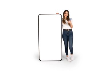 Akıllı telefon modeline yaslanırken cep telefonu kullanmak. Koca vücutlu, beyaz bir kadın, kocaman bir telefonun yanında duruyor. Yeni uygulama, web sitesi reklam pankartı fikri imajı. Boşluğu kopyala.