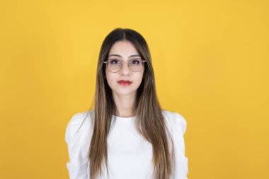 Kendine güvenen bir bayan, uzun kahverengi saçlı, sakin, yüzünde ciddi bir yüz ifadesi olan beyaz bir kadının portresi. Sarı stüdyo arka planında duruyor, kopyalama alanı. Modern 20 'lerin iş kadını konsepti.