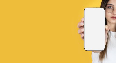 Uygulama reklam pankartı tasarım fikri. Beyaz tenli, uzun kahverengi saçlı kadın boş ekran, modern akıllı telefon modeli gösteriyor. Bulanık yüz, telefona özenli odaklanma. Boşluğu kopyala.