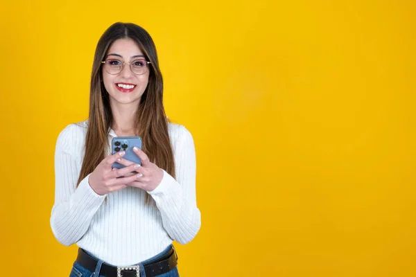 Woman using mobile phone, caucasian positive pretty woman using mobile phone. Enjoy distant communication, holding smartphone, surfing internet, dressed casual, isolated yellow background, copy space.