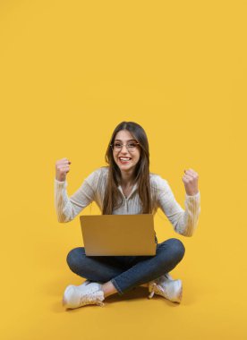 Kazanan poz, uzun vücut görünümü tatlı bir kızın zafer pozu vermesi. Modern dizüstü bilgisayarı tutuyor, iki yumruğu havada. Beyaz kadın zafer kavramını kutluyor. Boşluğu kopyala.