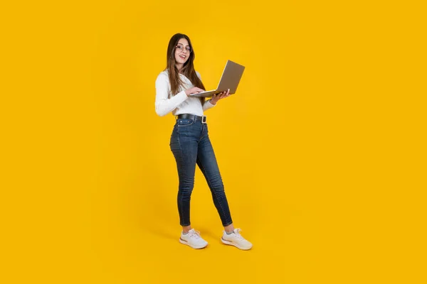 Full length side body view woman holding modern laptop. Young businesswoman wearing  jeans and white shirt. Office worker employee using computer. Caucasian long brown haired beautiful teenage girl.