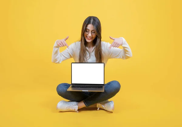 Pointing empty blank laptop screen, full length body view caucasian woman sitting floor pointing empty blank laptop screen. Modern notebook mockup. Female recommending website concept idea design.