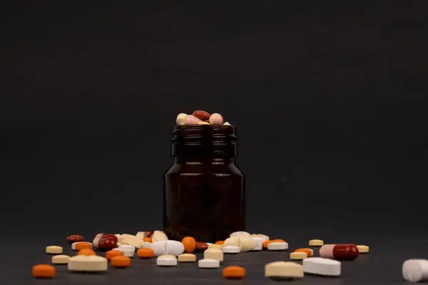 フルオレンジの薬瓶と黒の背景に周りの複数の異なる色の錠剤をこぼした コピースペース 白のカプセル 錠剤や薬 ビタミンサプリメントの概念のアイデア — ストック写真