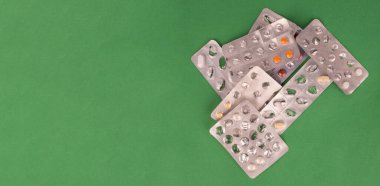 Açılmış kabarcık paketleri, birçok açık su toplayan paketin üst görünümü. Kronik hastalıklar, afiş fikri. İzole edilmiş yeşil arkaplan, kopyalama alanı. Tedavi, ilave renkli haplar, haplar.