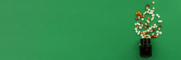 薬の錠剤の山 トップビューバナーのコンセプト薬の山 カラフルな薬の暗いガラス瓶の流出した 健康管理 緑の背景 コピースペース 抗生物質耐性 — ストック写真