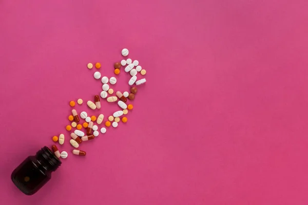 マルチカラータブレット マルチカラータブレットのトップビュー薬局のコンセプトイメージ 薬はガラス瓶からこぼれ落ちた 孤立したピンクの背景 コピースペース 病気に対する鎮痛剤 — ストック写真