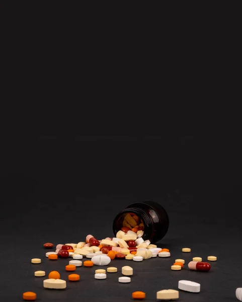 薬の丸薬 カラフルなこぼれた薬のフロントビューのイメージ コピースペースと隔離された豪華なコンセプト黒の背景 縦型広告のアイデア 治療の概念 — ストック写真