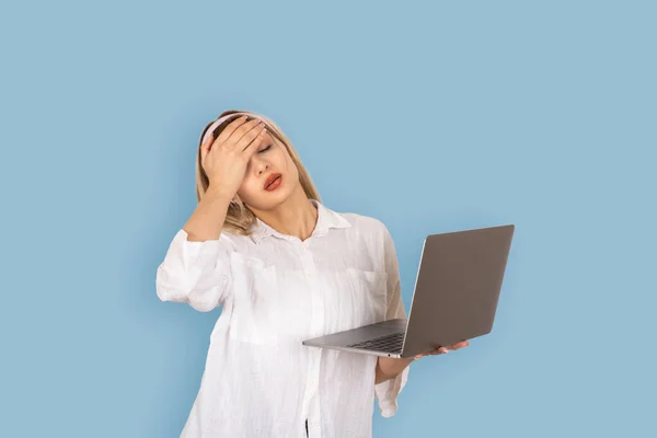 stock image Stressed woman holding laptop,  portrait of young blonde stressed woman holding laptop. Tired, exhausted with headache holding head with hand. Fear or upset for mistake concept idea. Isolated on blue.