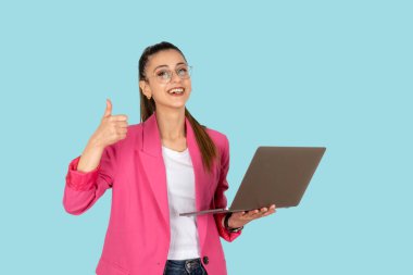 Genç esmer, iş kadını, klasik pembe ceketli, dizüstü bilgisayardan parmak kaldırma hareketi. Çevrimiçi bilgisayar sohbetini kullanarak, interneti tarayarak. İzole edilmiş mavi arkaplan, kopyalama alanı.