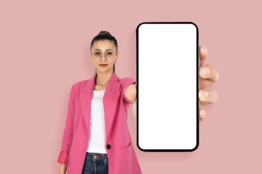 Mükemmel mobil uygulama, mükemmel mobil uygulama gösteren uzun saçlı esmer kızın portresi. Boş ekran maketi olan modern akıllı telefonu tutuyorum. Pembe ceket giy, kameraya bak..
