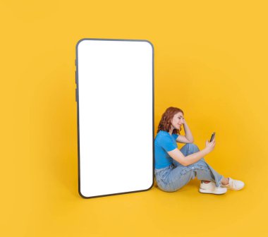 Kocaman boş ekran cep telefonu, gülümseyen mutlu kızıl saçlı beyaz kız kocaman boş ekran cep telefonunun maketini yapıyor. Akıllı telefon kullanan bir kız. Sarı arkaplan.