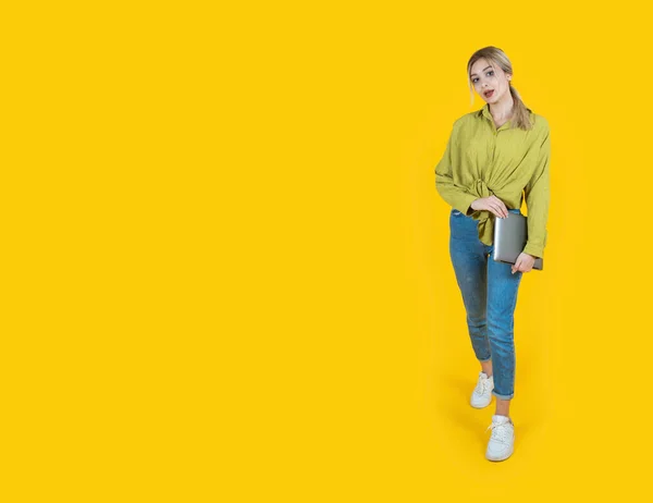 stock image Holding closed laptop, full body view young happy blonde girl holding closed laptop. IT worker, student, employee woman wear denim, green shirt. carrying notebook pc computer looking camera. 