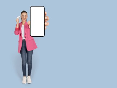 Çevrimiçi alışveriş uygulaması öneriliyor, tam vücut görünümü heyecanlı esmer kadın çevrimiçi alışveriş uygulaması öneriyor. Boş ekran cep telefonu modeli gösteriliyor. Kredi kartı, internet alışverişi, ikramiye.