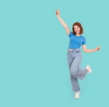 Neşeli, mutlu bir kadın, tüm vücudun önünde genç, neşeli, mutlu bir kadın. Kafkasyalı genç kız uzanmış elleri parmak ucunda dikiliyor. Sade mavi stüdyo arka plan fotokopi alanı. Yaşam tarzı kavramı.