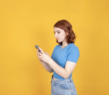 Akıllı telefondan yazmak, akıllı telefonda yazan genç bir kadının yan görünüm portresi. Cep telefonu iletişim fikri görüntüsü. Çevrimiçi uygulama kullanımı, internetten alışveriş, izole edilmiş sarı.