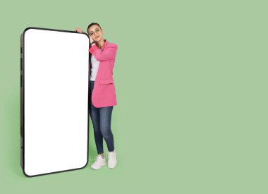 Mobil teklif, beyaz ekran modeli ile büyük bir akıllı cep telefonuna yaslanan beyaz saçlı genç esmer kız. Önerilen başvuru, web sitesi, tüm vücudu gören poz veren kadın. Alan reklamını kopyala.