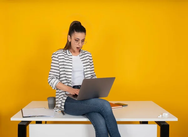 Young shocked woman office worker, portrait of caucasian pretty cute young shocked woman office worker. Sit at office desk, holding using laptop pc isolated yellow background studio. Business career.