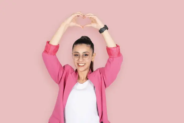 Girl shows hand heart gesture, portrait of young caucasian girl shows hand heart gesture top of her head above. Portrait of business woman happy smiling, standing over pink background. Copy space.