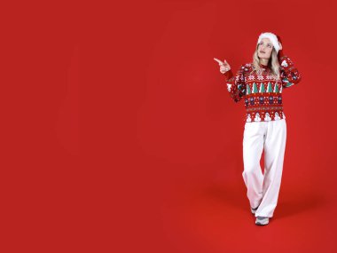 İşaret parmağı bir yana, geniş açılı ön görüş şaşkın bir şekilde Noel Baba kadını işaret parmağını bir kenara kaldırdı. Kopya alanı oluşturuluyor. Noel kazağı giy. Kırmızı renkli duvar arka plan stüdyosu.