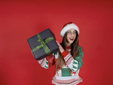 Kutlama tatili, Noel Baba 'nın heyecanlı bayramının portresi. Beyaz kız hediye kutusunu sallıyor, içinde ne olduğunu merak ediyor. Kırmızı Noel şapkası, Noel süveteri. Büyük siyah hediye kutusu.