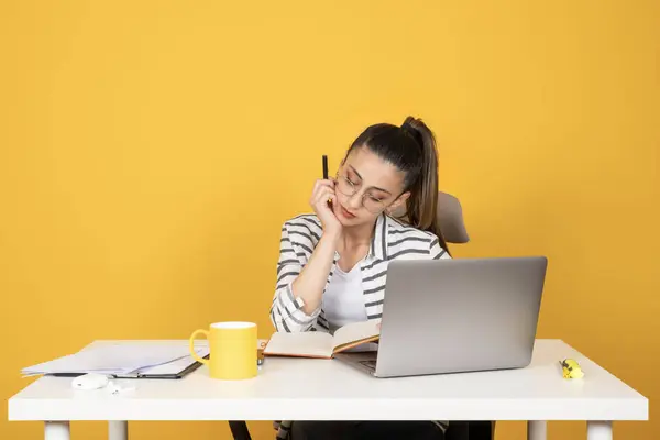 Businesswoman taking notes, portrait of young brunette caucasian businesswoman taking notes. Female office worker sit at desk, work on laptop reading. Isolated yellow studio background, copy space.