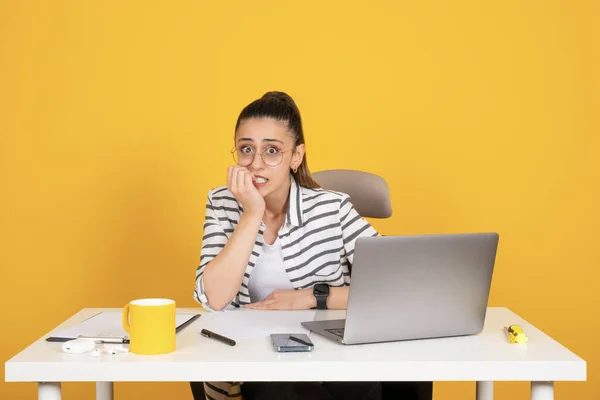 Female office worker sit at office desk wearing glasses looking afraid stressed and nervous. Businesswoman hand on mouth biting nails. Anxiety. Work on laptop. Business problems. Copy space.