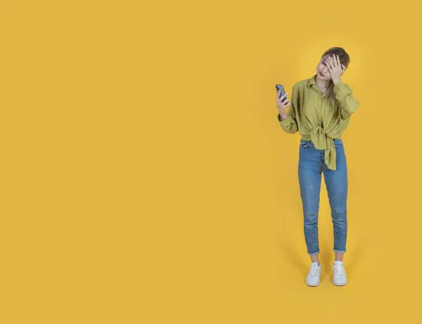 Sad young woman, full body length caucasian sad young woman. Desperately looking smartphone. Waiting good news. Feeling bad. Depressed, anxious student. Isolated yellow, copy space.