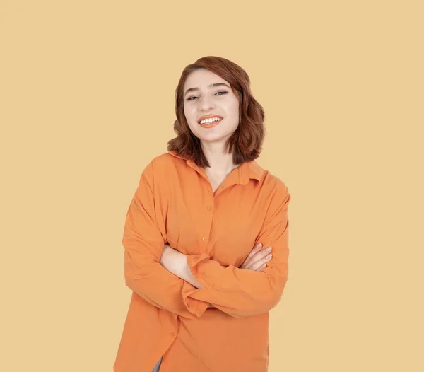 Smiling confident woman, young caucasian red bob haired smiling confident woman. Posing crossing arms, standing over pastel orange studio background. Happy, positive, proud lifestyle concept.