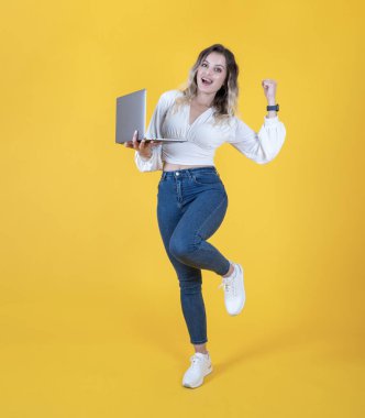 Tam vücut heyecanlı mutlu öğrenci ya da sıradan kot pantolon giyen IT 'ci kadın beyaz gömlek tutun iş bilgisayarını kullanın kazanan kişi sarı izole edilmiş stüdyo arka planı yapsın. Uzayı kopyala Kazanmak için yumruğunu sık.