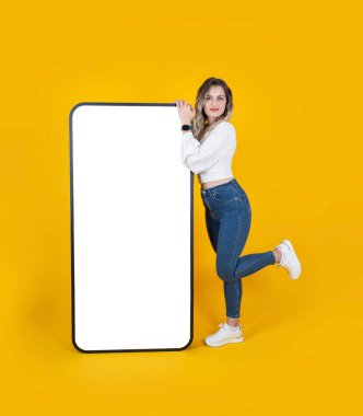 Büyük, büyük bir cep telefonu modeli. Uzun boylu, beyaz bir kadın. Kocaman bir cep telefonu modeli. Sarı stüdyo arka plan, kopyalama alanı. Web sitesi, uygulama reklamcılığı fikri.