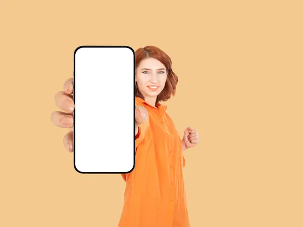 Young red bob hair cute charming woman hold hand mobile cell phone with blank empty white screen mock up show close up to camera. Selective focus on hand. Smiling, clenching fist. Recommending concept