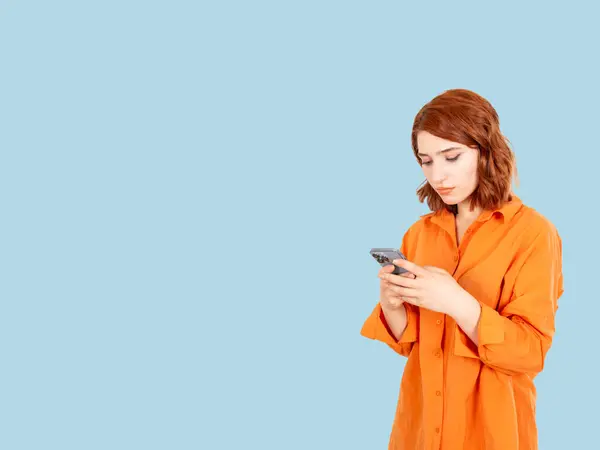 Serious woman using mobile phone, portrait of caucasian red bob hair serious woman using mobile phone. Sad girl hold use smartphone checking online, messaging, reading bad news. Blue background.