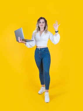 İyi niyet göstergesi, tüm vücut uzunluğu, güzel beyaz kadın dizüstü bilgisayar tutuyor ve iyi niyet gösteriyor. Günlük beyaz gömlek, kot pantolon ve beyaz spor ayakkabı giy. Sarı arkaplan, boşluğu kopyala.