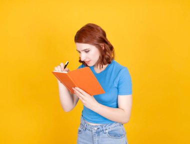 Not alıyorum, beyaz bir kadının portresi. Elinde turuncu kaplı defter tutuyordu. Sarı arka planda duran kalem kullanıyordu. Ödev yapmak, çalışmak. Boşluğu kopyala.